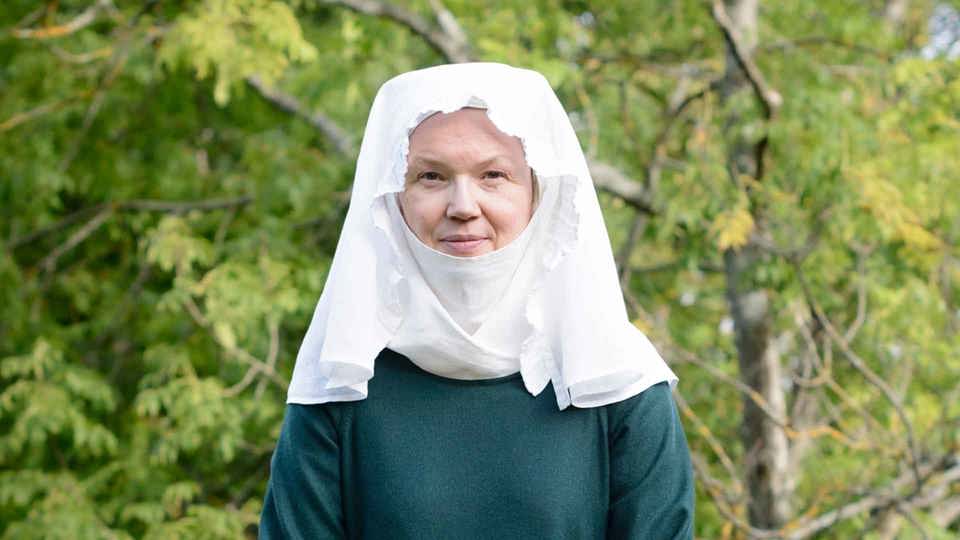 En kvinna klädd i vit huvudduk och mörkgrön helkroppsdräkt.