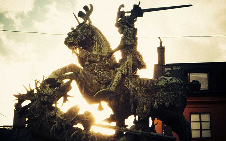 Riddare med draget svärd till häst hugger mot en drake.