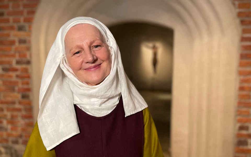 Kvinna i medeltida kläder utanför en kuliss av en medeltida kyrka.