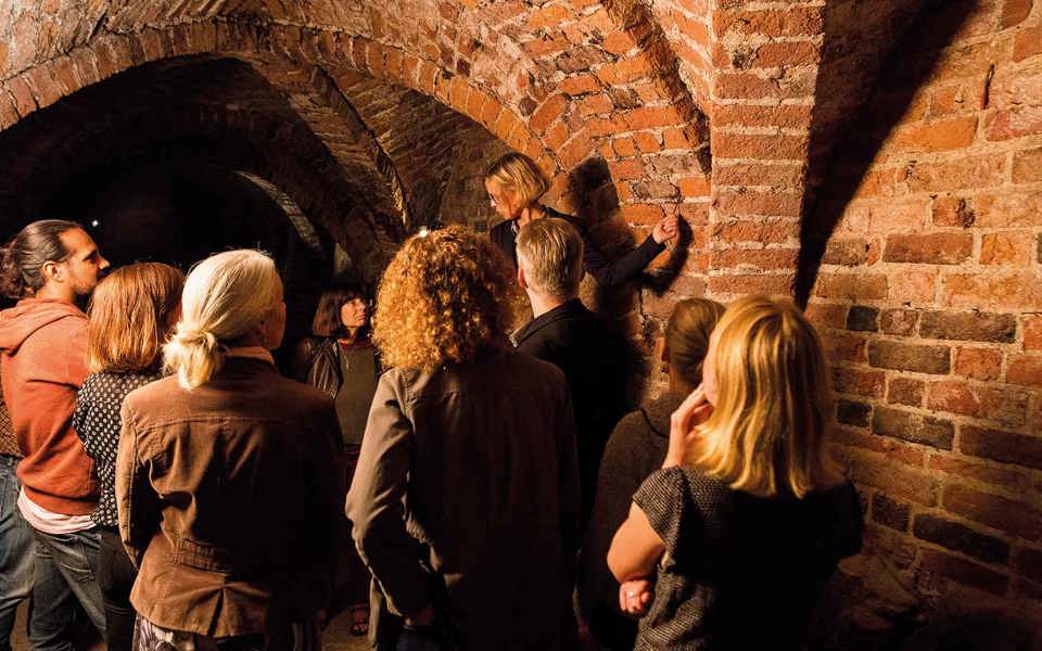 En guide visar ett medeltida tegelvalv för en grupp besökare.